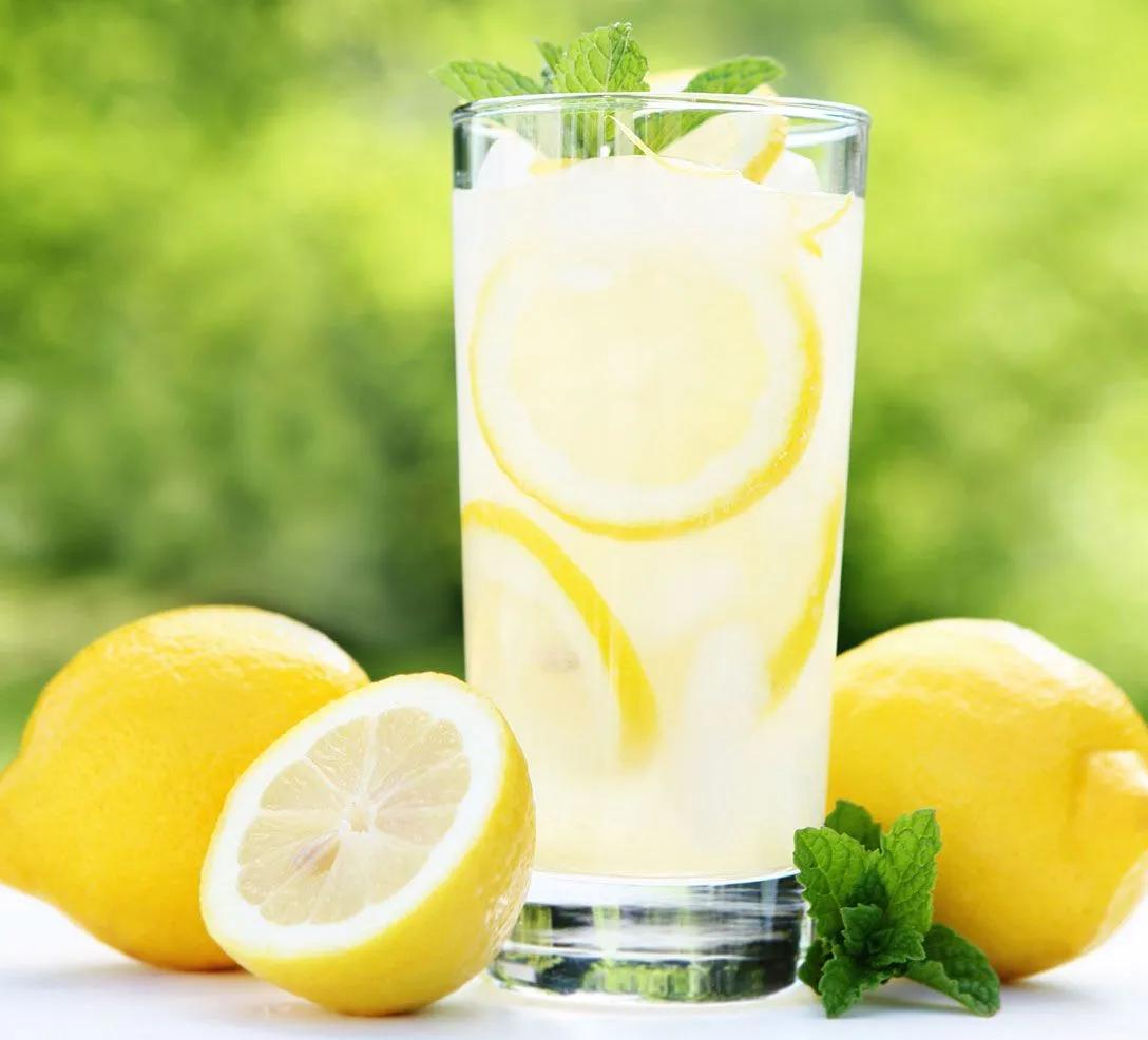 a glass filled with lemonade sitting next to two lemons and mint sprigs