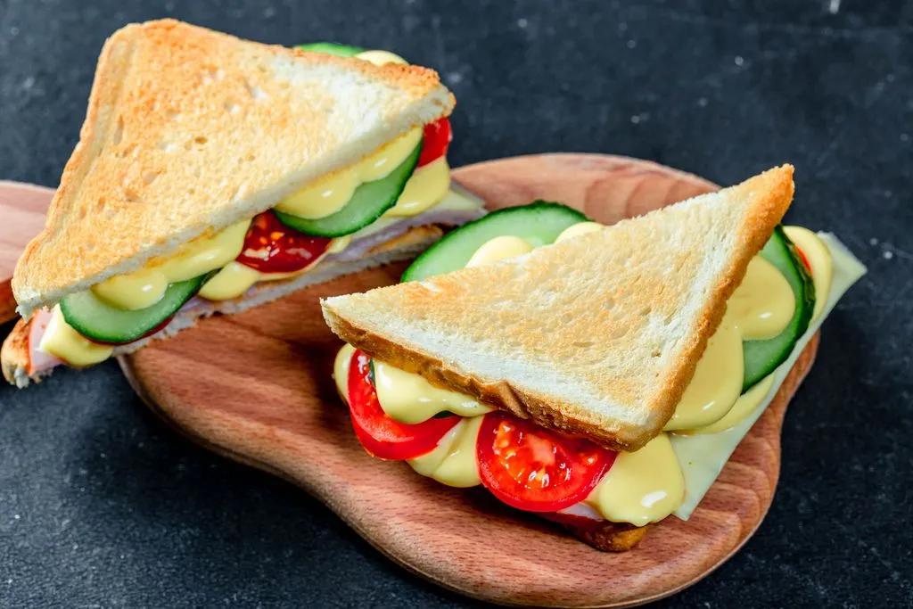 Two sandwiches with ham, cheese, tomatoes, lettuce, and toasted bread ...