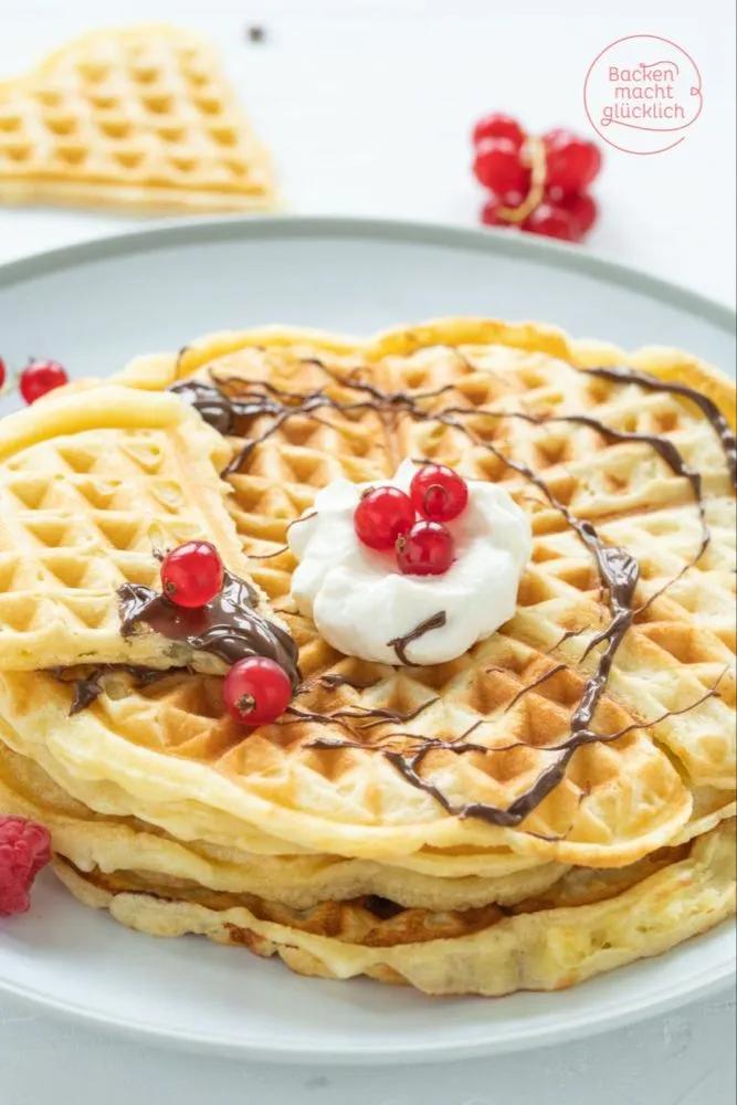 two waffles with whipped cream and cherries on top, sitting on a plate
