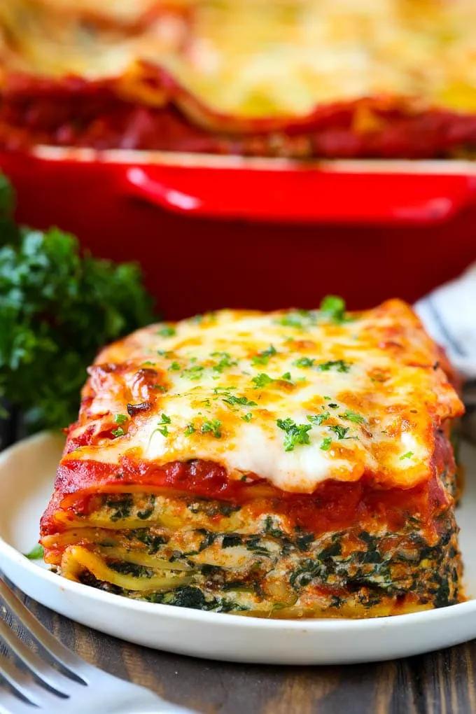 A piece of spinach lasagna on a plate, garnished with chopped parsley ...